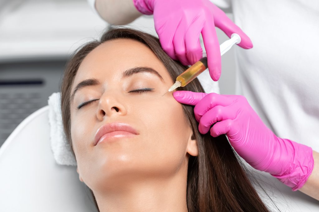 Mezoterapia igłowa, kosmetyczka nakłuwa twarz kobiety.